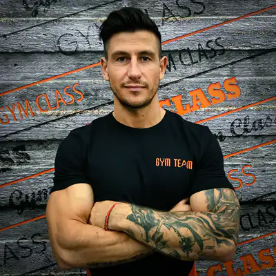 Edző karba tett kézzel, tetoválás, edzőterem fal.